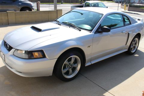 2002 Ford Mustang - A silver 2002 Ford Mustang GT coupe is seen from the front 3/4 angle, with a pickup truck in the background.