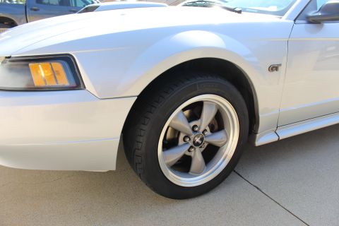 2002 Ford Mustang - Close-up of a silver Ford Mustang GT's front wheel and fender, with a truck visible in the background.
