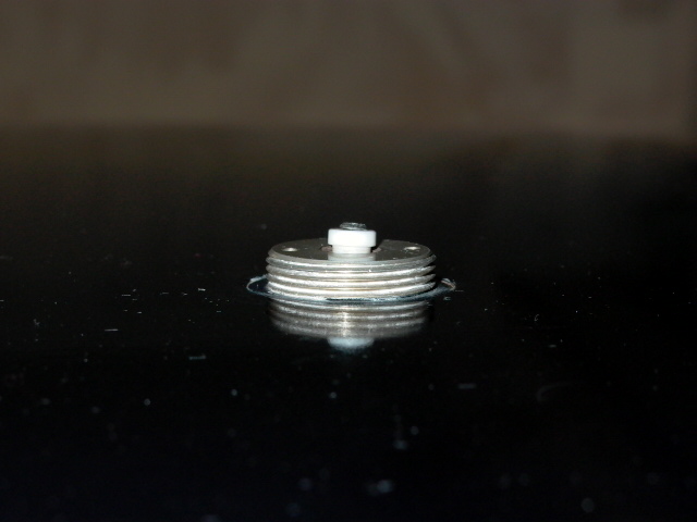 Metal part with stacked discs and a white plastic center, possibly a valve or cap