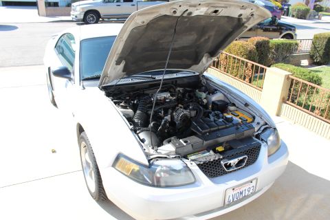 2002 Ford Mustang - A white 2002 Ford Mustang is shown from the front with its hood open, displaying the engine compartment. Another vehicle is visible in the…