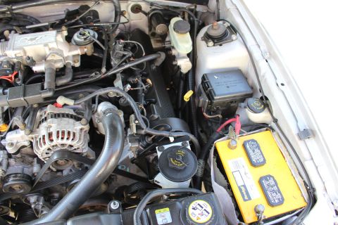2002 Ford Mustang - Close-up view of a car's engine bay, a yellow battery and alternator.