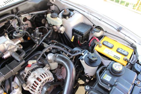 2002 Ford Mustang - The engine bay of a vehicle, a yellow battery, alternator, and numerous hoses and electrical components.