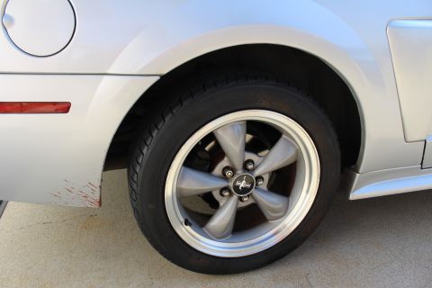 2002 Ford Mustang - Close-up of a silver Ford Mustang's rear wheel and fender, showing some red paint scuffs near the taillight.