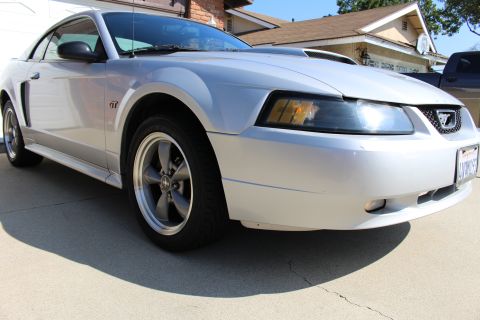 2002 Ford Mustang - Silver Ford Mustang GT with a hood scoop and GT badging is parked in front of a house.