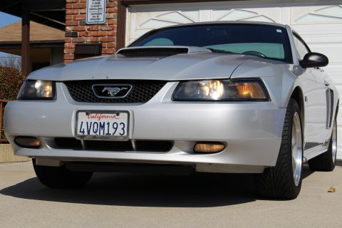 2002 Ford Mustang - A silver 2002 Ford Mustang is parked in front of a garage, displaying its front grille and license plate.