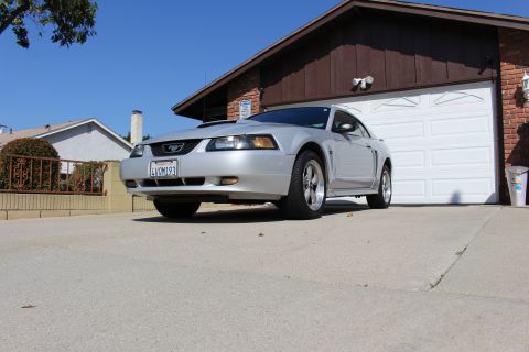 2002 Ford Mustang - A silver Ford Mustang is parked in front of a suburban garage on a sunny day.