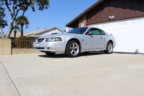 2002 Ford Mustang - Silver coupe with a hood scoop and aftermarket wheels parked in a residential driveway.