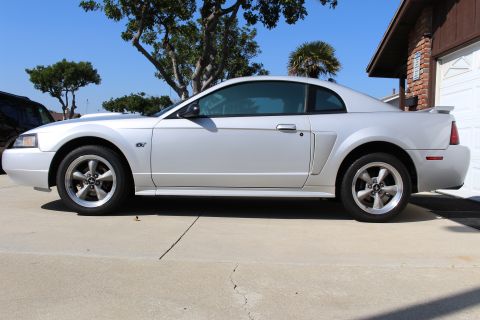 2002 Ford Mustang - Silver Ford Mustang coupe with a GT badge is parked on a concrete driveway.