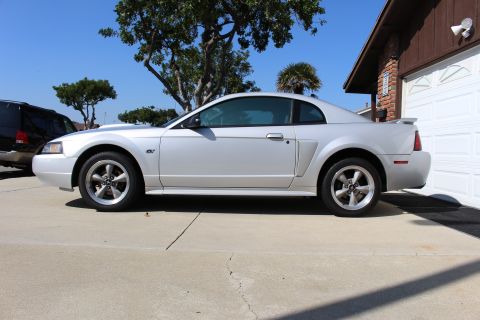 2002 Ford Mustang - Side view of a silver 2002 Ford Mustang GT coupe parked in front of a garage.