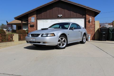 2002 Ford Mustang - A silver 2002 Ford Mustang is parked in front of a garage, with a clear blue sky overhead.