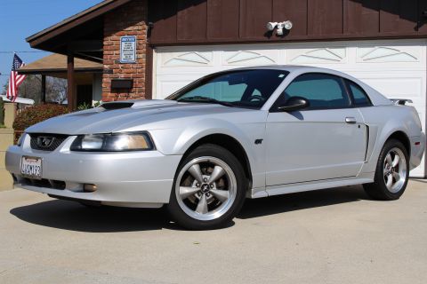 2002 Ford Mustang - A silver 2002 Ford Mustang GT is parked in front of a suburban garage. The car has a prominent hood scoop.