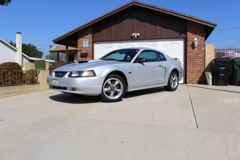 2002 Ford Mustang - A silver Ford Mustang is parked in a driveway in front of a house and garage.