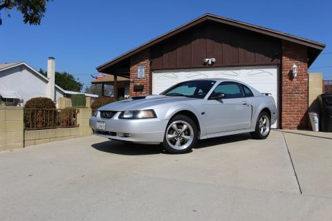 2002 Ford Mustang - A silver 2002 Ford Mustang coupe is parked in a driveway in front of a house and garage.