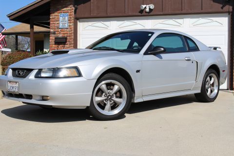 2002 Ford Mustang - A silver 2002 Ford Mustang GT coupe is parked in front of a brick house and garage.