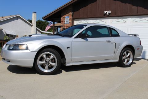 2002 Ford Mustang - This silver Ford Mustang GT is parked in front of a suburban garage on a sunny day.
