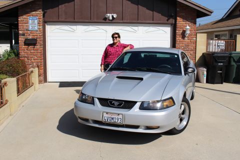 2002 Ford Mustang - A silver 2002 Ford Mustang is parked in front of a garage with a person leaning on it.