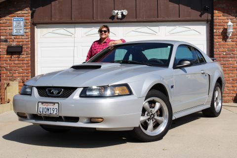 2002 Ford Mustang - A silver 2002 Ford Mustang is parked in front of a brick garage with a person leaning on it.