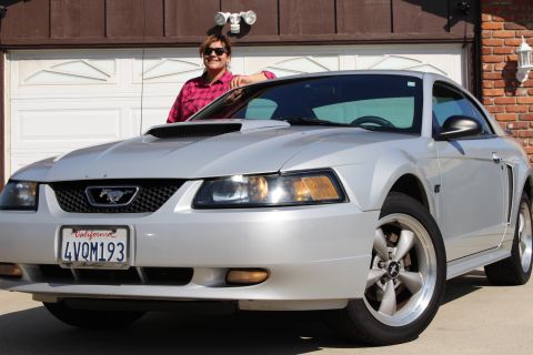 2002 Ford Mustang - A silver 2002 Ford Mustang is parked in front of a garage with a woman leaning on the car.