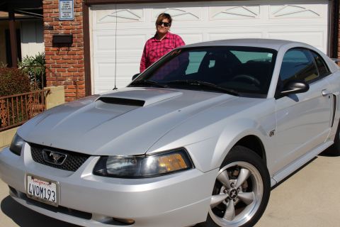 2002 Ford Mustang - A silver 2002 Ford Mustang GT is parked in front of a garage, with a person standing behind the car.