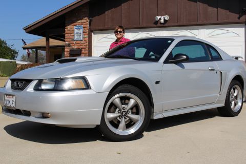 2002 Ford Mustang - A silver 2002 Ford Mustang GT coupe is parked in front of a garage with a woman standing behind it.