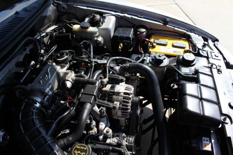 2002 Ford Mustang - Close-up of a 2002 Ford Mustang engine, highlighting the intricate mechanical components and a prominent yellow battery.