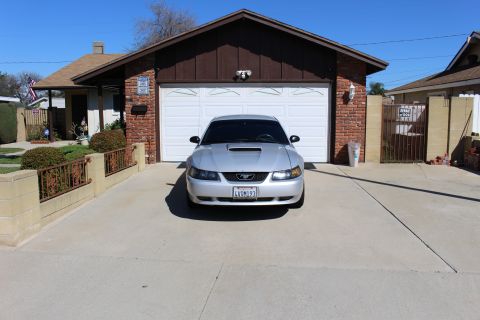 2002 Ford Mustang - A silver 2002 Ford Mustang is parked in front of a garage on a sunny day.