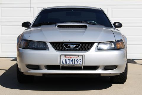 2002 Ford Mustang - A silver 2002 Ford Mustang is parked in front of a garage door, showing its front grille and headlights.