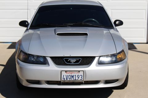 2002 Ford Mustang - A silver 2002 Ford Mustang is parked in front of a garage door, showing its front grille and hood scoop.