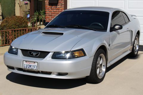 2002 Ford Mustang - A silver 2002 Ford Mustang coupe is parked in front of a garage, a hood scoop and aftermarket wheels.
