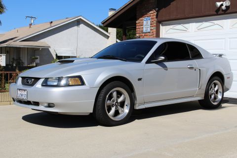 2002 Ford Mustang - Silver 2002 Ford Mustang GT with a hood scoop and GT badging is parked in front of a garage.