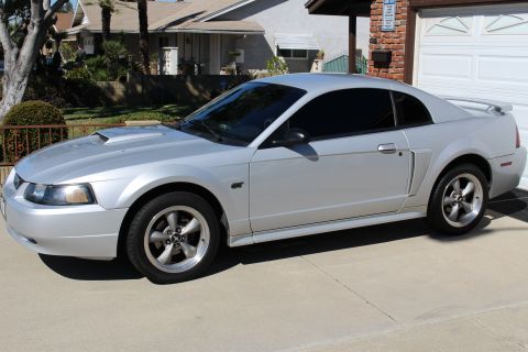 2002 Ford Mustang - A silver 2002 Ford Mustang coupe is shown from the side with tinted windows and a hood scoop.