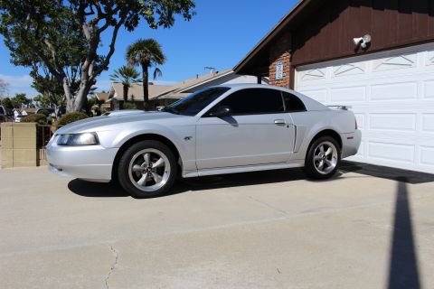 2002 Ford Mustang - A silver 2002 Ford Mustang coupe is parked in front of a garage on a sunny day.