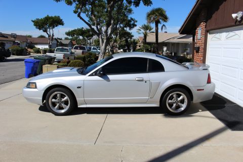 2002 Ford Mustang - A silver 2002 Ford Mustang is parked in front of a garage on a sunny day.