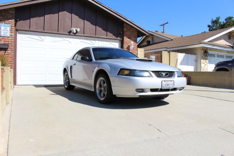 2002 Ford Mustang - A silver 2002 Ford Mustang coupe is parked in front of a garage, a prominent hood scoop.