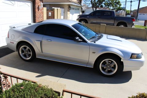 2002 Ford Mustang - Silver 2002 Ford Mustang GT coupe parked in driveway with a dark pickup truck behind a wall.