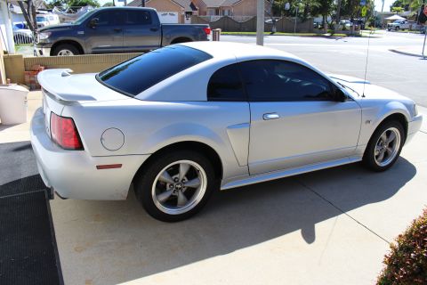 2002 Ford Mustang - A silver Ford Mustang coupe is seen from a three-quarter front angle, parked on a driveway with a pickup truck in the background.