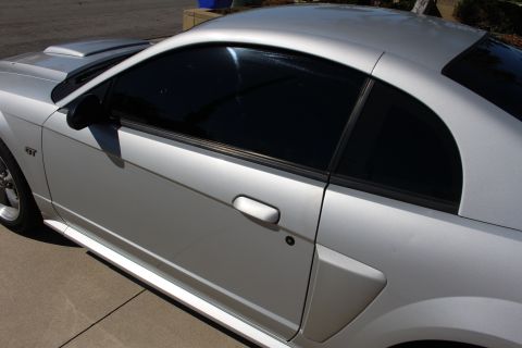 2002 Ford Mustang - The side profile of a silver Ford Mustang shows its tinted windows and GT badging.