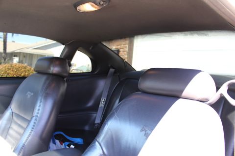 2002 Ford Mustang - The interior of a 2002 Ford Mustang is visible, black leather seats with embossed horse logos and a view of the exterior through the window…