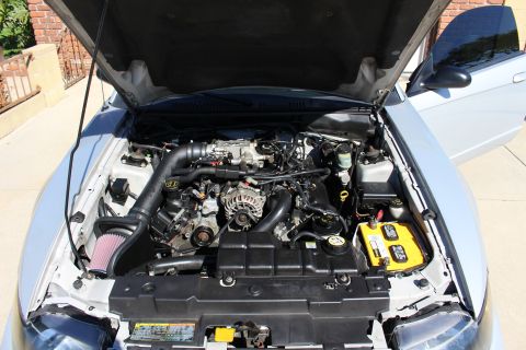 2002 Ford Mustang - The engine bay of a silver 2002 Ford Mustang is visible with the hood open, revealing the V8 engine and aftermarket modifications.