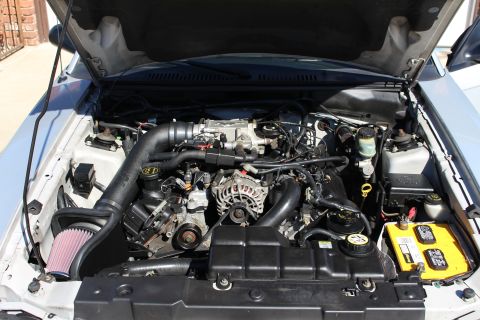 2002 Ford Mustang - Engine bay of a 2002 Ford Mustang an aftermarket cold air intake and a yellow battery.