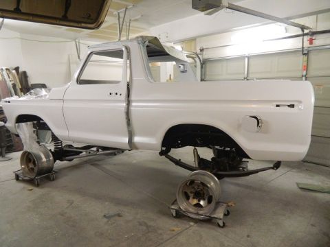 1979 Ford Bronco - The body of a white pickup truck is suspended in a garage, appearing to be in the process of restoration.