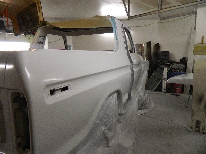 Ford Bronco body, primed and covered in plastic, in a garage. Doors and roof are open