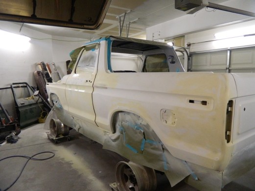 1978 Ford Bronco body undergoing bodywork, covered in primer and masking tape