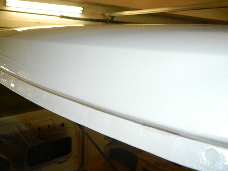 Close-up of white paint on the inside of a vehicle's roofline, showing some texture. Interior structure is visible below
