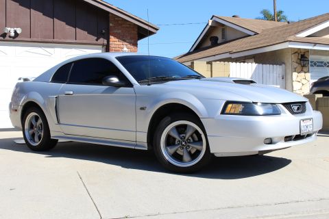 2002 Ford Mustang - A silver 2002 Ford Mustang GT is parked in front of a suburban house on a sunny day.