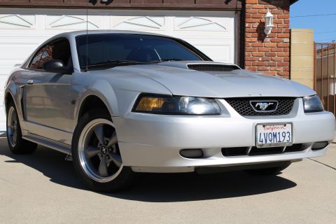 2002 Ford Mustang - Silver 2002 Ford Mustang coupe with a California license plate parked in front of a brick garage.