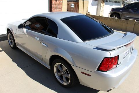 2002 Ford Mustang - A silver 2002 Ford Mustang is parked in a driveway with tinted windows and a rear spoiler.