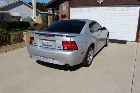 2002 Ford Mustang - This silver 2002 Ford Mustang features a rear spoiler and tinted windows, parked in a suburban driveway.