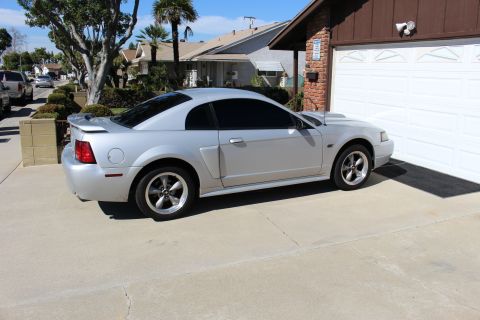 2002 Ford Mustang - A silver 2002 Ford Mustang coupe is parked in a residential driveway next to a garage.