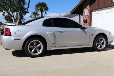 2002 Ford Mustang - Silver 2002 Ford Mustang with tinted windows and a rear spoiler is parked in front of a garage.